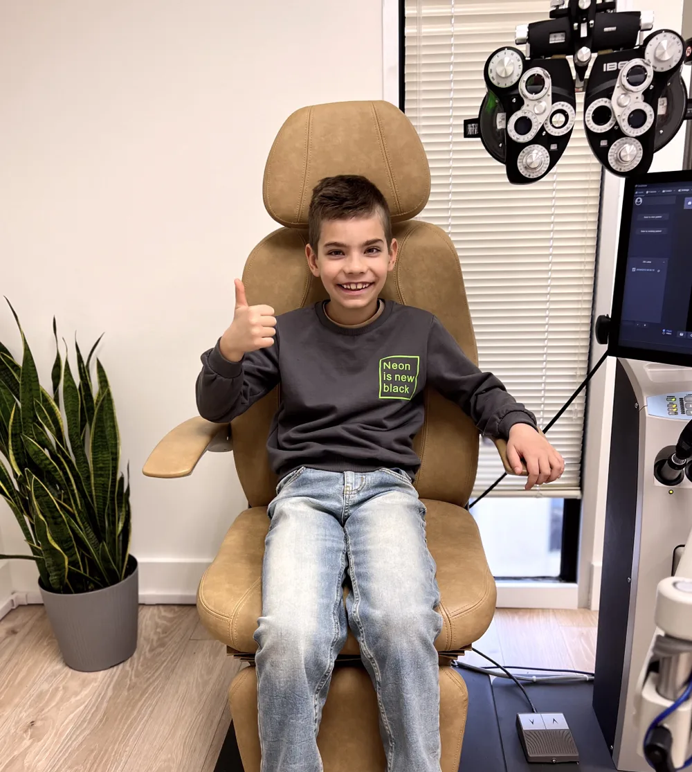 Young patient smiling and giving a thumbs up in optometry chair